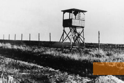 Bild:Westerbork, o.D., Stacheldraht und einer der sieben Wachtürme des Lagers, Herinneringscentrum Kamp Westerbork/NIOD